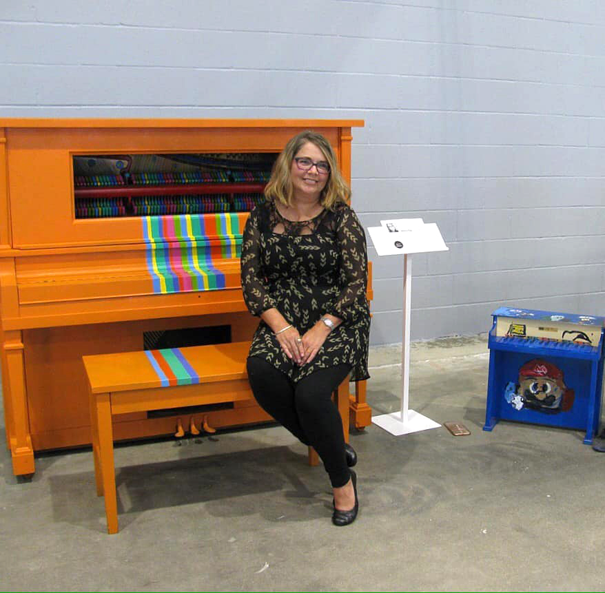 Denise King poses with her finished piano, titled Chromesthesia, at at Madjax's Second Thursday event on July 11, 2019. Photo provided