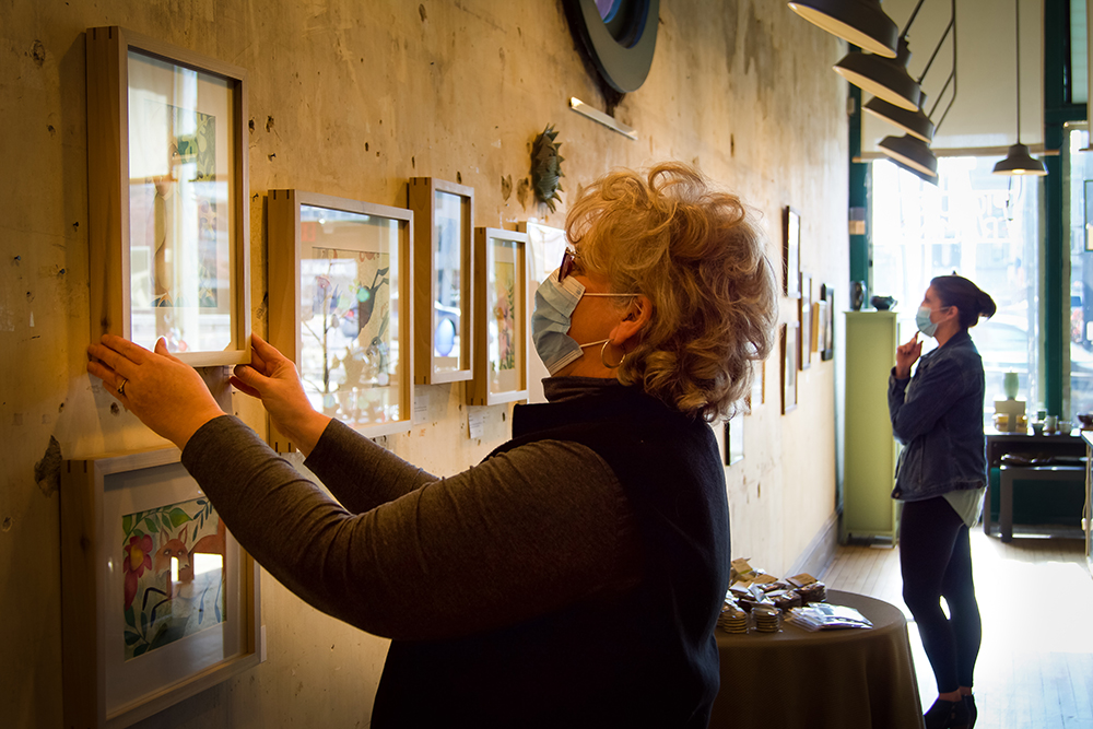 Barbara Schaefer hangs a new piece of artwork in the art gallery. Photo by Matt Howell.