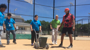 Scott Smalstig (green shirt) guides TeenWorks kids on the fine art of operating a line marker device on a ball field. Photo provided