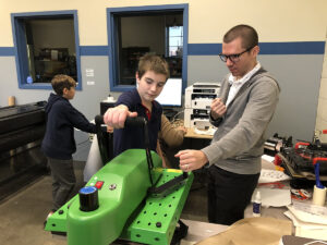 Instructor James Lodl helps a student use a heat press to create a personalized pet tag at a Pet Productions workshop. Photo by Emily Helms