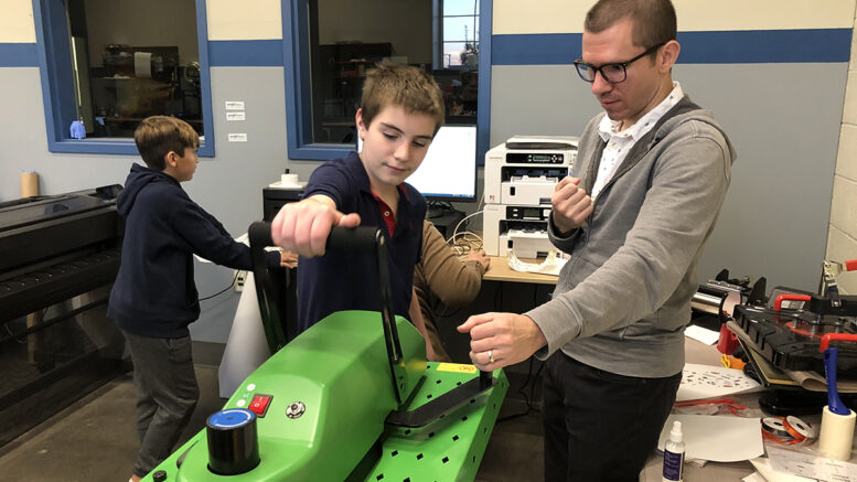 Instructor James Lodl helps a student use a heat press to create a personalized pet tag at a Pet Productions workshop. Photo by Emily Helms