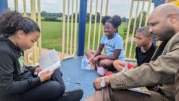 Longfellow Elementary School student Isabella Foster reads Charlotte’s Web to Longfellow Principal Gerry Moore and her schoolmates A’Nyiah Shannon and Rashaud Hill.