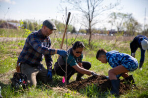 Chris Allen holds a tree in place while his wife, Christine, and son, Henry, shove dirt into the hole at Dutro-Ernst Woods, Saturday, April 22, 2023 in Muncie, Ind. Christine said she met her husband while volunteering and they both love hiking on Red-Tail properties, and they both wanted to teach their son the value of volunteering. Photo by Jaden Whiteman.